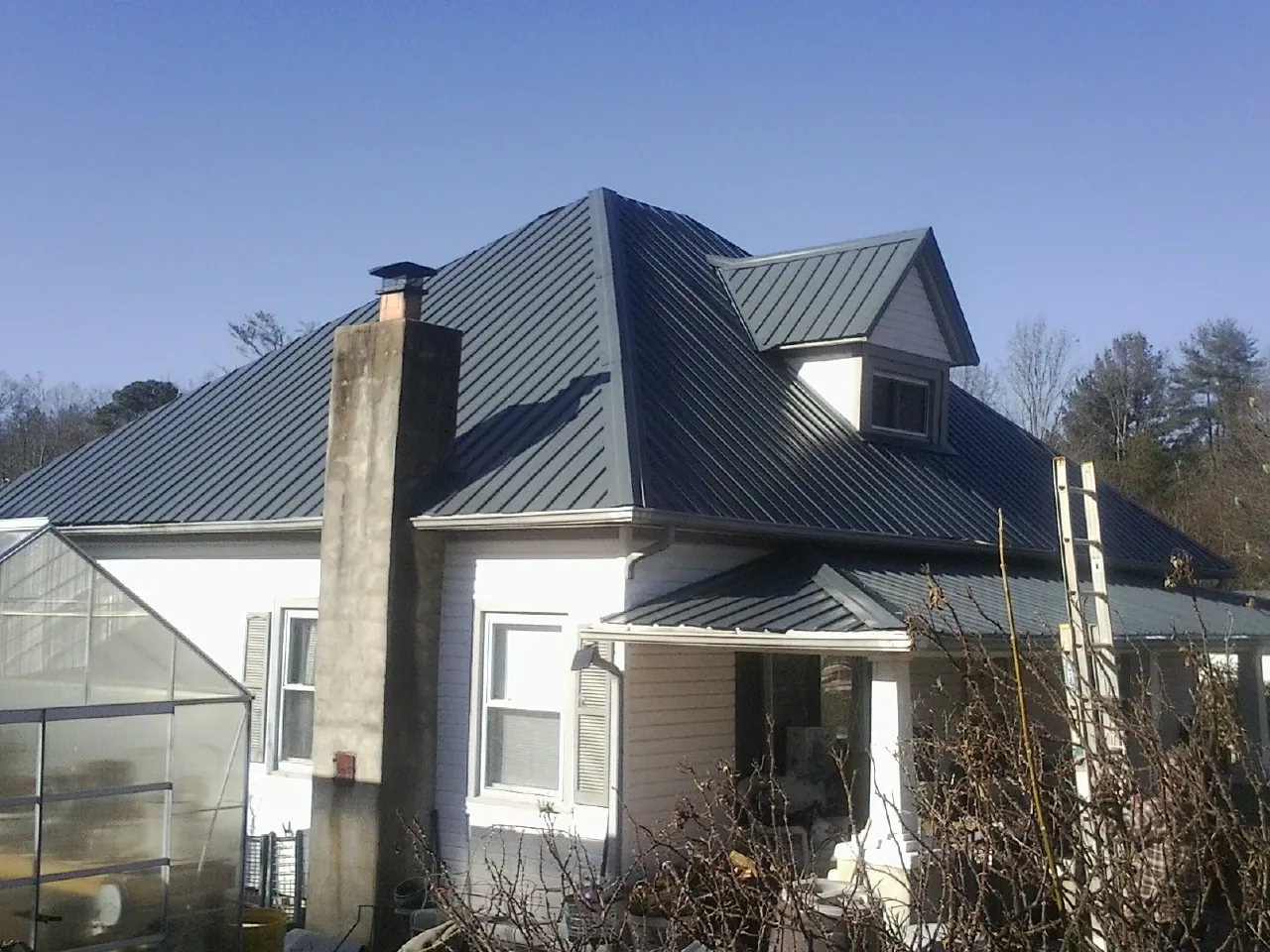 Dark blue standing seam metal roof on a white farmhouse with dormer — Slate & Tile Roof Repair by Roofing Brothers in New Eagle