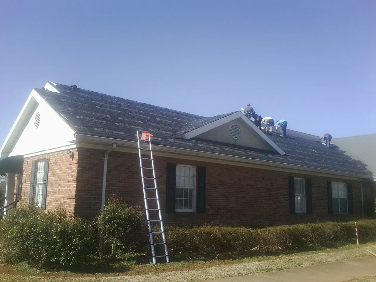 Crew tearing shingles off a brick ranch roof with a ladder set — Metal Roof Repair work by our crew in New Eagle