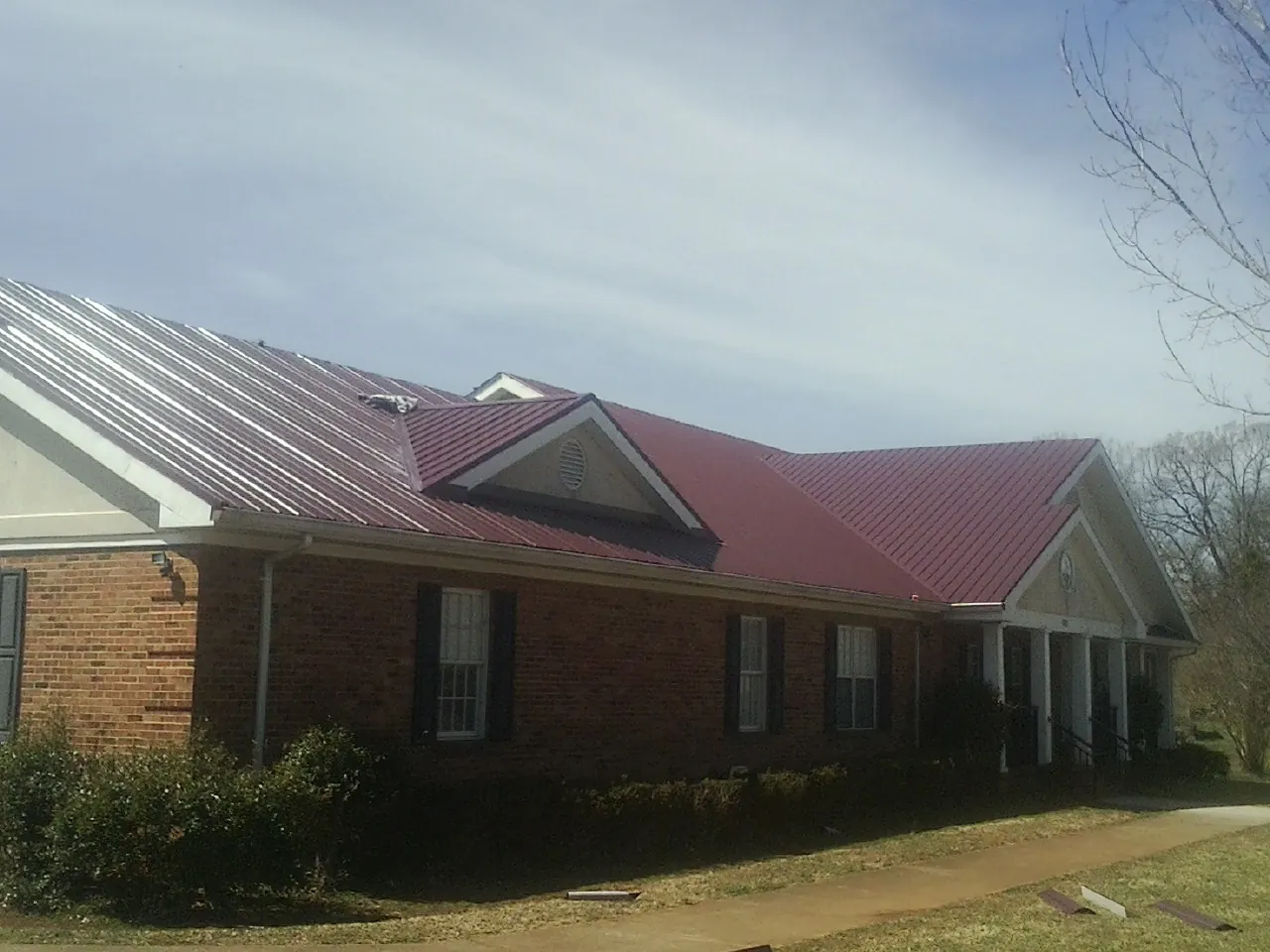 Red metal roof with gabled entries on a long brick building, from a Hail Damage Roof Repair job in New Eagle