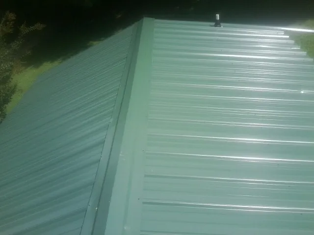 New green metal panels meeting at the ridge of a roof — Flat Roof Repair work by our crew in New Eagle