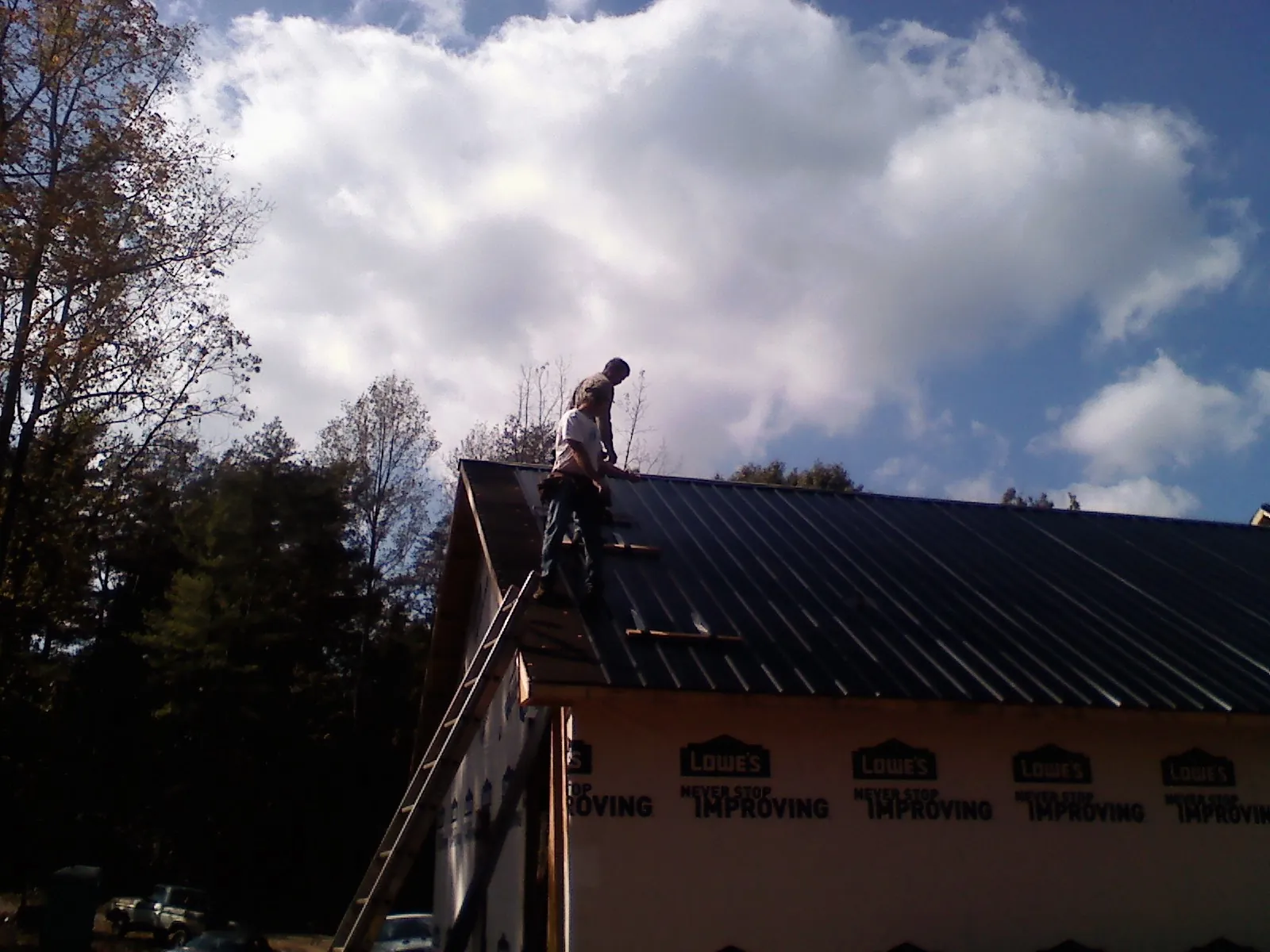 Roofer fastening dark metal panels high against a cloudy sky, from a Roof Inspection job in New Eagle