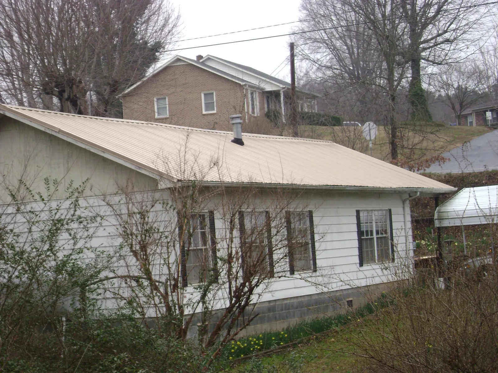 Tan metal roof on a white sided house set into a hillside — Commercial Roofing by Roofing Brothers in New Eagle