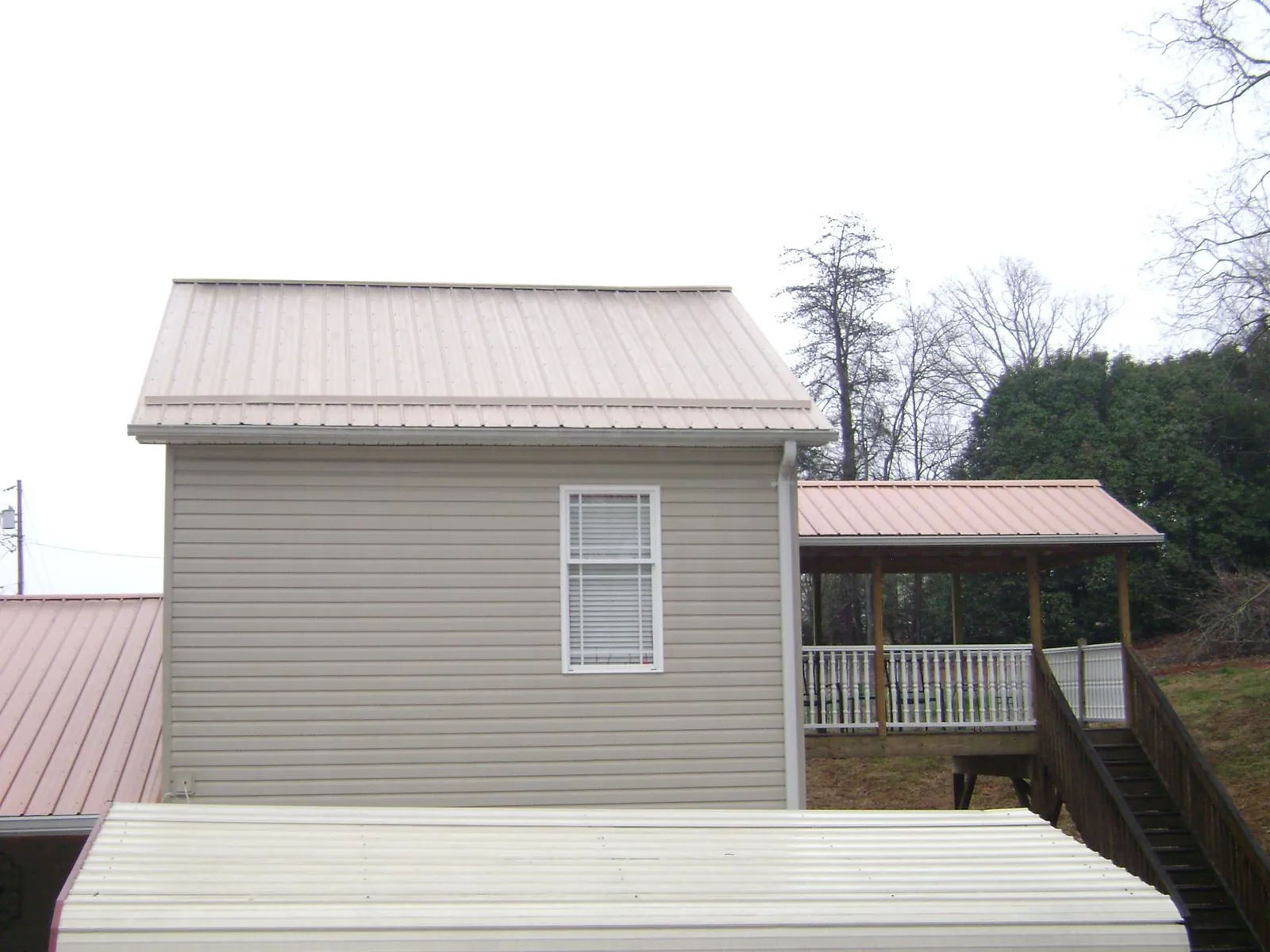 Tan metal roofs on a two story addition and attached porch, from a Roof Replacement job in New Eagle